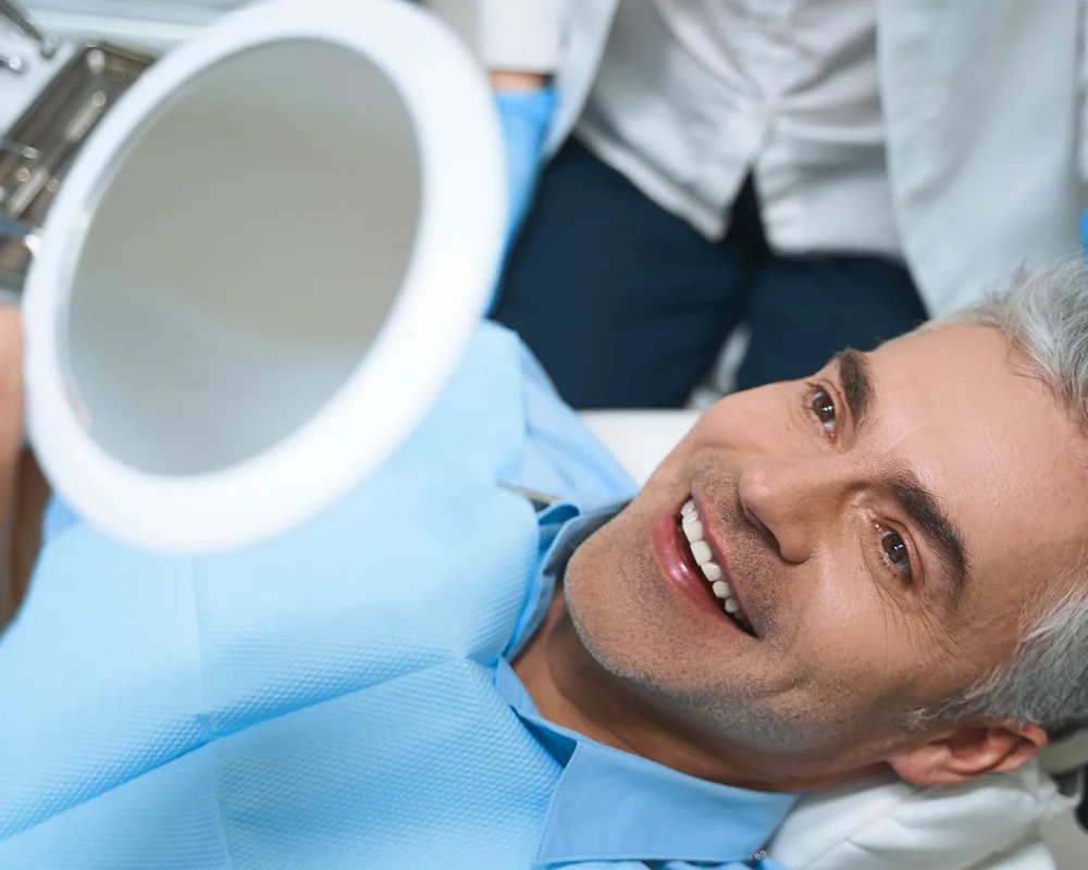 Uomo brizzolato sulla poltrona del dentista che si guarda i denti